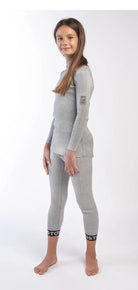 Ein junges Mädchen mit langen braunen Haaren steht barfuß vor einem weißen Hintergrund, trägt das Diston DISTON Cut Resistant Top Junior - 4FIS Stars in CRG - CORE / Racing Fit und passende Leggings mit schwarzen Bündchen, posiert und lächelt leicht in die Kamera.