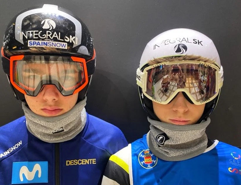 Zwei junge Athleten mit Skihelm, Skibrille und Diston DISTON Cut Resistant Neck Guard (4 FIS Sterne, CORE/Racing Fit) stehen Seite an Seite und zeigen ihr Engagement für den Skirennsport und die Sicherheit auf der Piste.