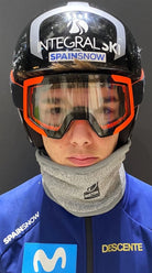 Eine Person trägt einen schwarzen Skihelm mit INTEGRALSKI SPAINSNOW Branding, eine orange Skibrille, einen Diston DISTON Cut Resistant Neck Guard (4 FIS Sterne in CRG - CORE/Racing Fit) und eine blaue DESCENTE x SPAINSNOW Jacke - ideal für den Skirennlauf.