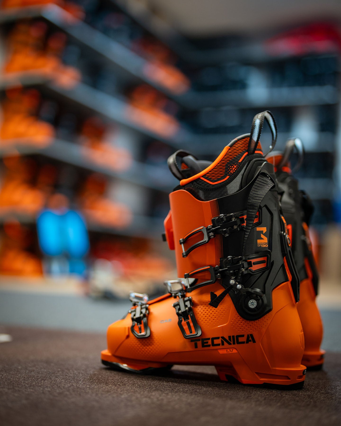 Tecnica Skischuhe Mach 1 LV 130 in leuchtendem Orange auf Ausstellungsflaeche im Sportfachgeschaeft – hochwertige Skischuhe fuer anspruchsvolle Skifahrer mit optimaler Passform und Performance.