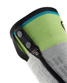 Eine Nahaufnahme eines grau-grünen Strickärmels mit zwei schwarzen Druckknöpfen und schwarzem Besatz, der ein Etikett mit goldenem Text und einem blauen Streifen aufweist. Inspiriert von den SIDAS Ski Race S.E.T. Socken, spiegelt es die Qualität von Sidas wider.